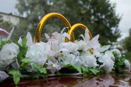 Closeup shot of a wedding arrangement made with white artificial flowers and golden rings.の写真素材