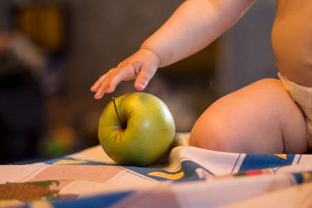 Closeup shot of a green apple lying on the table. Baby is trying to touch it.の写真素材