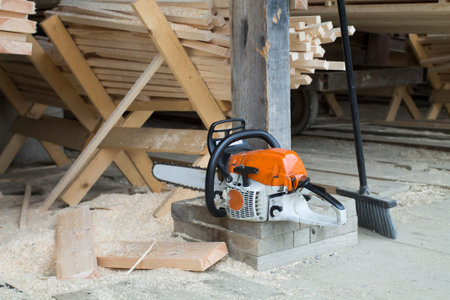 Motor chainsaw is left by the cut wooden planks in the sawmill area.の写真素材