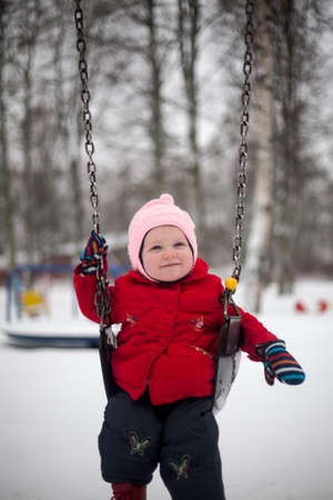 Smiling little girl is sitting on swings in winter day.の写真素材