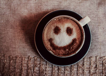 Photo of coffee cup of cappuccino on a saucer with print a smile on foam on a fabric napkin. Close-up view from top photoの写真素材