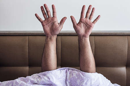 Male hands with open palms lifted up out of bed in bedroom. Rest and sleepの写真素材