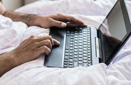 Close up of young male hands fingers working in bed on laptop typing on keyboard. Business work at homeの写真素材