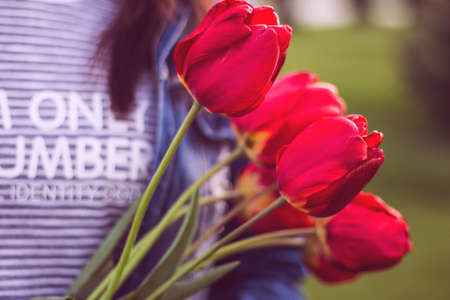 Young girl with bouquet of tulips flowers walks in park with green grass. Love and lifestyle