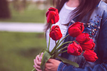 Young girl with bouquet of tulips flowers walks in park with green grass. Love and lifestyleの写真素材