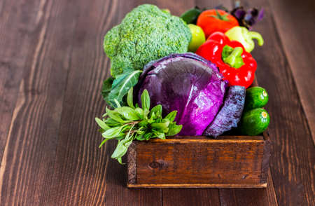 Fresh vegetables red cabbage and broccoli, cucumbers and peppers, tomatoes and basil in box on dark wooden background. Farm organic products. Horizontal photoの写真素材