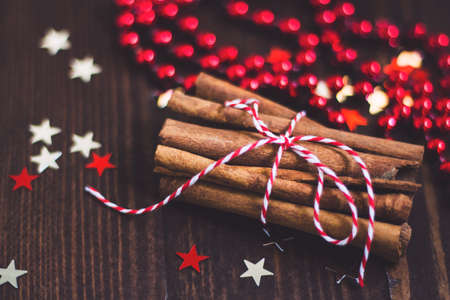Christmas cinnamon sticks tied with rope on wooden festive holiday table decorated with stars and red beads. Delicious spices for holiday baking cooking pastryの写真素材