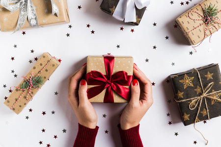 Woman hands holding christmas holiday gift box red bow on decorated festive table with sparkle stars...