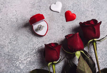 Valentines day marry me wedding engagement ring in box with red rose gift surprise on grey background with copyspace. Love flower gift for woman making proposal on romantic holiday weddingの写真素材