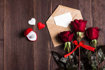 Valentines day envelope love letter with greeting card engagement ring in box mothers day red rose gift surprise on dark wooden background with copyspace. Love flower gift for woman romanticの写真素材