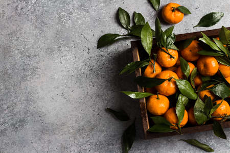Tangerines with green leaves in wooden box on light background. Orange mandarins sweet fresh citrus fruit healthy food. Horizontal photo top viewの写真素材