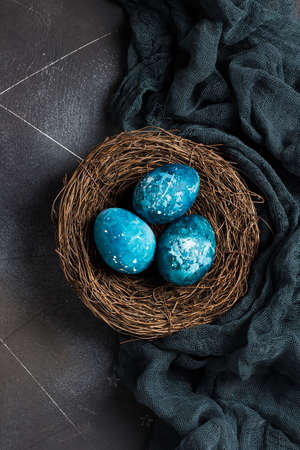 Easter eggs in nest painted by hand in blue color on dark background. Chicken eggs catholic and orthodox easter holidayの写真素材