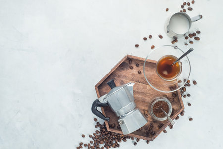Wooden tray with Moka pot, espresso cup, ground coffee jar and coffee beans on a white concrete background with copy space. Header with brewing coffee ingredients.の写真素材