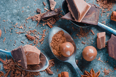 Teaspoons of cocoa, dark and milk chocolate, cinnamon, spices and round chocolates on a stone background. Making a dessert. Macro food photography with copy space. Ingredients close-up.の写真素材