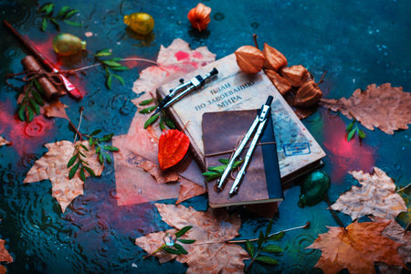 Rainy autumn still life with books, fallen leaves, drawing compasses, papers and water drops on a...
