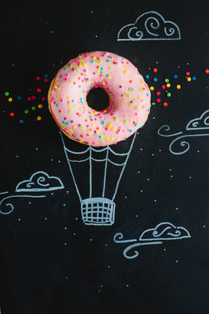 Pink glazed donut with chalk drawing of hot air balloon. Creative concept. Low key food photography.の写真素材