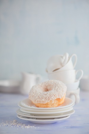 White donut with coconut topping on a light background with porcelain cups and saucers. High key food photography. Stack of tableware.の写真素材