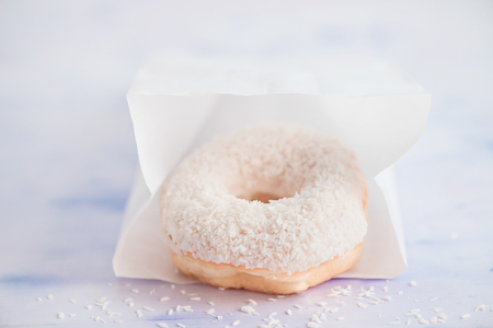 Close-up of a white donut with coconut topping on a light background inside paper delivery packaging. High key food photography.の写真素材