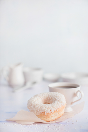Tea time scene. White donut with coconut topping on a light background. High key food photography. Cup of tea with dessert.の写真素材