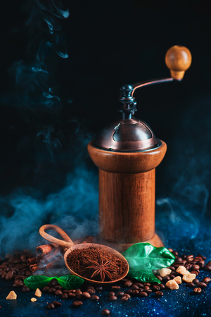 Roasted coffee beans with steam and coffee grinder on a dark background. Arabica leaves, brown sugar and anise stars as spices. Vintage still life with hot drink.の写真素材