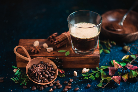 Espresso shot with foam on a wooden box with coffee beans, arabica leaves, cinnamon and spices on dark background. Brewing coffee still life.の写真素材