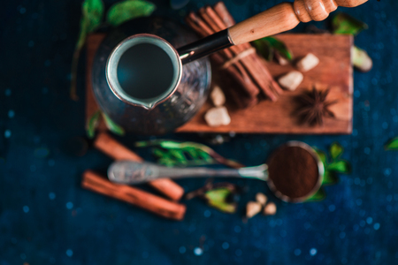 Flat lay with cezve, beans, cinnamon and spoon of ground coffee on a wooden background. Brewing coffee concept with copy space.の写真素材