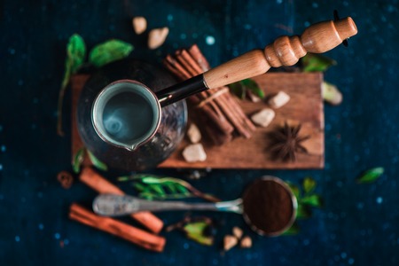 Steaming cezve with hot coffee on dark background with beans and cinnamon. Top view of coffee preparation process.の写真素材