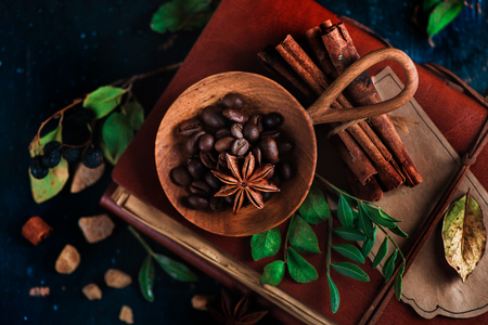 Wooden bowl with coffee beans on a dark background with anise stars, cinnamon, brown sugar and leaves. Vintage still life with barista utensils. Brewing coffee concept with copy space.の写真素材