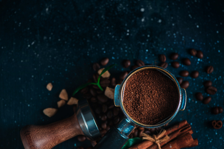 Coffee making equipment with copy space. Portafilter with ground coffee, tamper, cinnamon and beans on a dark wooden background.の写真素材