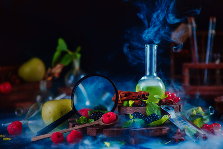 Nutritionist workplace with laboratory tubes, green smoothie, magnifying glass and assorted berries, raspberry  with mint leaves. Dark food photography, science concept. Copy space.の写真素材