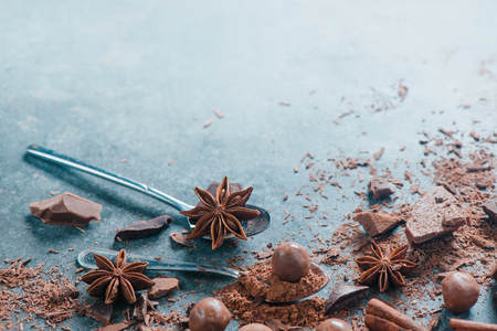 Teaspoons of cocoa, dark and milk chocolate, cinnamon, spices and round chocolates on a stone background. Making a dessert. Macro food photography with copy space. Ingredients close-up.の写真素材