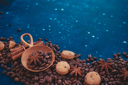 Scattered coffee beans with handmaiden wooden scoop, cinnamon, anise stars and cookies on a dark background. Header or title image with copy space.の写真素材