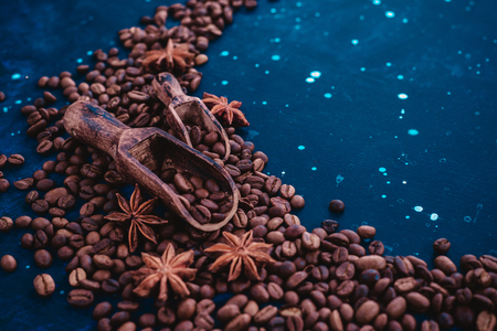 Close-up of two wooden scoops for coffee beans with cinnamon and anise stars on a dark blue background. Vintage barista concept.の写真素材