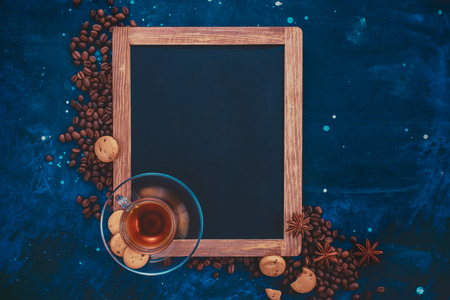 Glass coffee cup on a blank blackboard frame with coffee beans, cinnamon, spices and cookies. Creative chalk lettering concept for barista.の写真素材