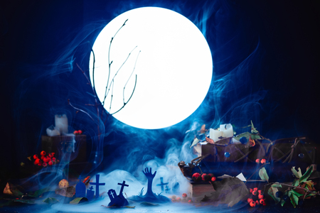 Graveyard with rising zombies silhouettes in full moon light. Conceptual Halloween still life with smoke, dry branches, candles and magical equipment. Zombie apocalypse wallpaper.の写真素材