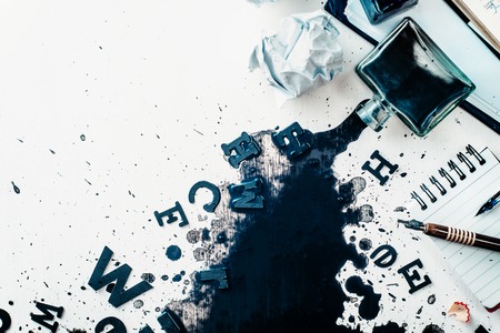 Header with spilled ink, crumpled paper, scattered letters, papers and notepads on a white wooden background. Creative writing concept. Flat lay with copy space. High key still life with an inkwell.の写真素材