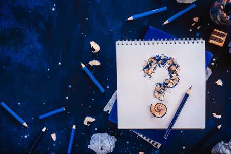 Question mark from pencil shavings with crumpled paper balls, pencils, notepads and empty coffee...