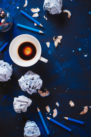 Dark background with crumpled paper balls, empty coffee cups, pencils, paper, notes and notepads. Still life with writer workplace. Creative writing concept.の写真素材
