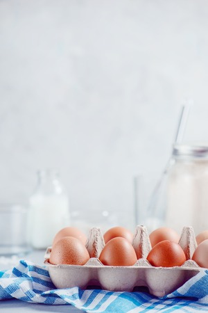 Eggs in a paper tray on a light background with milk, flour and ingredients for Easter cooking. High key background with copy space.の写真素材