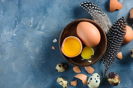 Yolk in an eggshell close-up. Raw cooking ingredients background with copy space. Modern Easter concept with brown hen eggs and feathersの写真素材