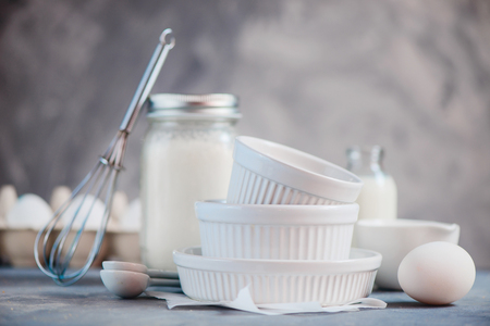 Porcelain baking forms in cooking concept with eggs, flour, and milk on a concrete background. High key food photography with copy space.の写真素材