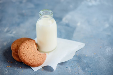 Cookies with bite marks and a bottle of milk on a light blue kitchen table with copy space. Healthy breakfast minimalist concept.の写真素材