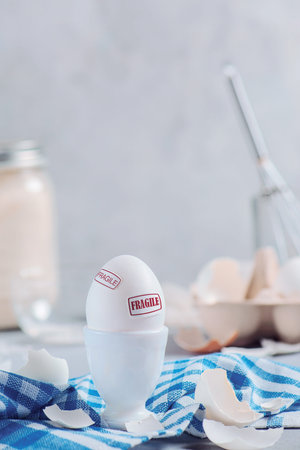 White egg in a porcelain egg stand with a red Fragile sign. High key background with copy space....