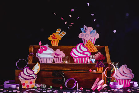 Colorful cupcakes collection on a wooden shelf with confetti and sprinkles. Papercraft dessert assortment a dark background with copy space.の写真素材