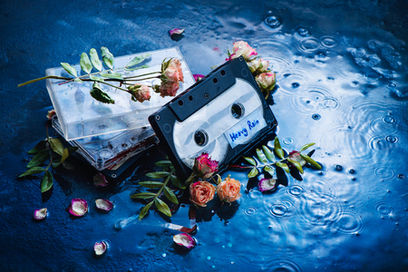 Audio cassette tape with Heavy Rain label in a scene with rose petals and raindrops. Melancholy music for rainy weather. Nostalgia concept copy space.の写真素材