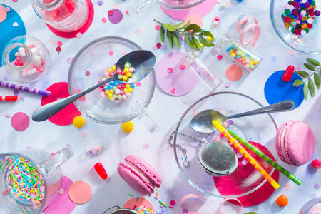 Sprinkles, confetti, candies, macaroons and birthday candles on a white background. Glass transparent tea cups from above.の写真素材