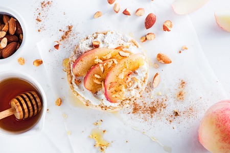 Crisp bread snack with caramelized peach slices, soft creme cheese, almond, cinnamon, honey. Healthy breakfast concept in a high key.の写真素材