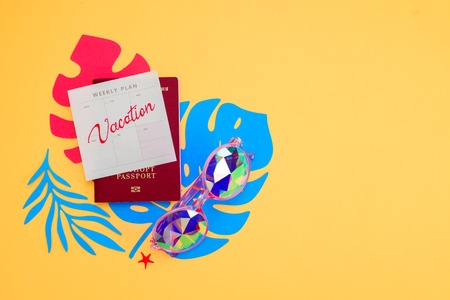 Summer vacation flat lay with beach accessories and tropical leaves on a vibrant yellow background. Travel essentials from above with copy space. Modern colorful palette.の写真素材