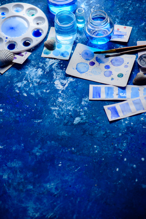 Artist workplace with watercolor sketches in shades of blue. Monochromatic painting with glass jars, paint and brushes. Drawing sea concept with copy space.の写真素材