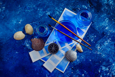 Creative artist workplace with marine watercolor, palettes, swatches, brushes and water jars from above. Painting sea concept on a navy blue background with copy space.の写真素材